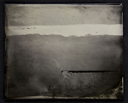 C2: Landscape photo on glass becomes field of warm/cool tonal ranges. Warm grey on top. Dark grey dominates below. Demarcated by a silver streak