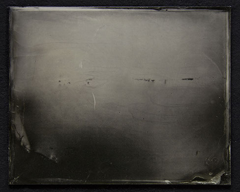 C3: Landscape photo on glassplate. Medium cool greys above-Dark warm grey below. Small dark scrapes as image or photochemical residue. U decide.