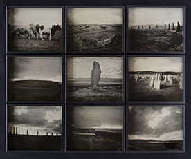 A 3x3 grid of glass photographs on black velvet in matte black frames. Depict Orkney landscapes of grassy hills, monoliths, cows, graves & shore
