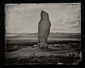 Panel B2-an ancient monolith center in the frame surrounded by swirls of grass, clouds & hills both shadowy & brightly lit. Low Horizon line.